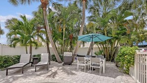 Une terrasse extérieure avec une piscine, des chaises longues, un barbecue et des palmiers.