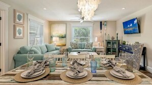 Un coin repas avec une table dressée pour quatre personnes, un lustre et un téléviseur fixé au mur.