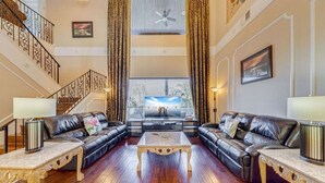 A spacious living room with a high ceiling, a staircase, and a large window with a view.