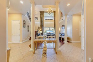 Enter a grand space with a central table, flanked by columns, and a staircase leading to a seating area.