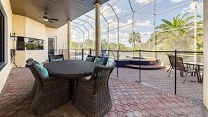 A covered patio with wicker furniture, a pool, and a view of palm trees.