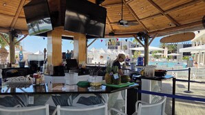 Zona de bar con techo de madera, un televisor y vistas a una piscina y edificios al fondo.