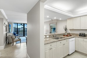 A modern kitchen with granite countertops, a dishwasher, and a dining area with a chair and table. - On the Beach, Sundial of Sanibel, Gulf View Premium Condo, Oct/Nov. discounts! (Sanibel)
