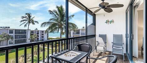 A balcony with a table and chairs, a ceiling fan, and a view of palm trees and buildings.