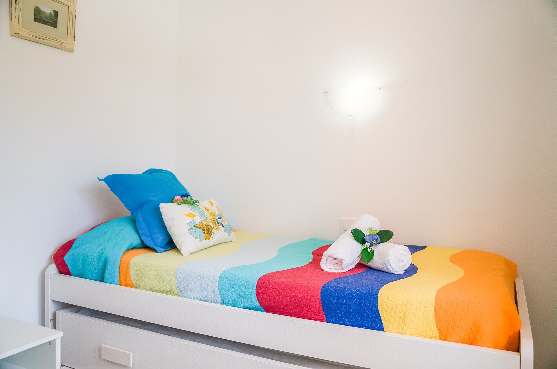 A bed with a colorful quilt, a blue pillow, and a decorative pillow with a floral design.