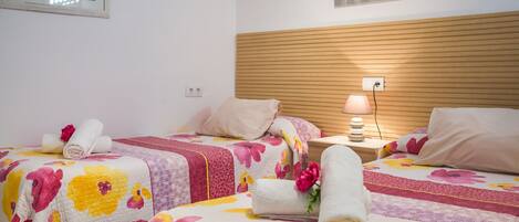 Habitació d'hotel amb dos llits, roba de llit floral, un panell de fusta al capçal, una nit de nit amb una làmpada, i un quadre amb marc a la paret.