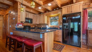 Cocina de cabaña de madera con una isla grande, taburetes de bar, un refrigerador y una ventana con vistas.