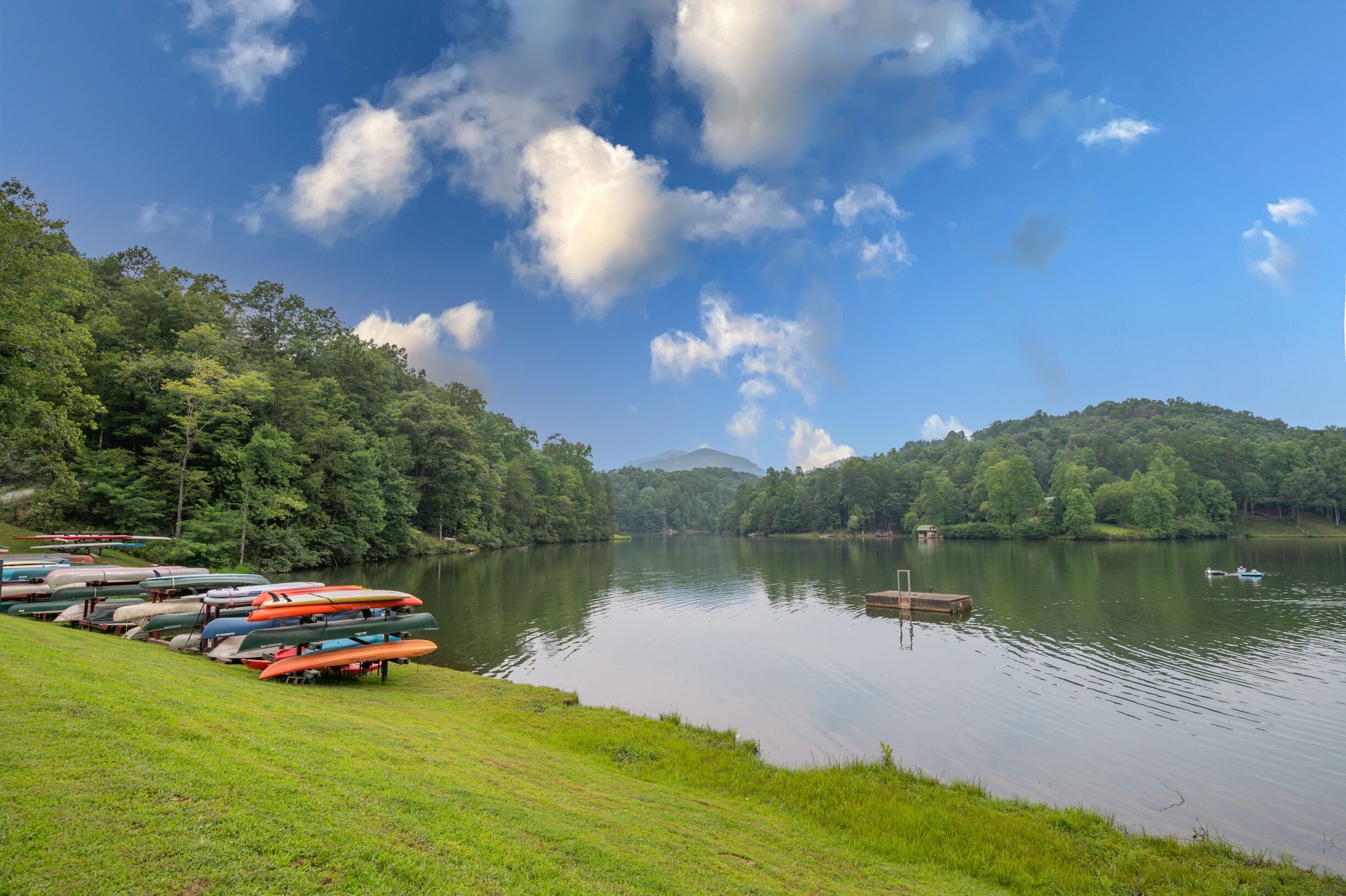 A calm lake with boats docked on the shore, surrounded by lush greenery and hills in the background.