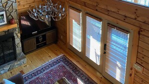 Una habitación de madera con techos altos, chimenea de piedra, araña y ventanas amplias.