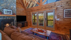 Interior acogedor de una cabaña de madera con chimenea de piedra, un amplio sofá de cuero, una mesa de centro de madera y un televisor.