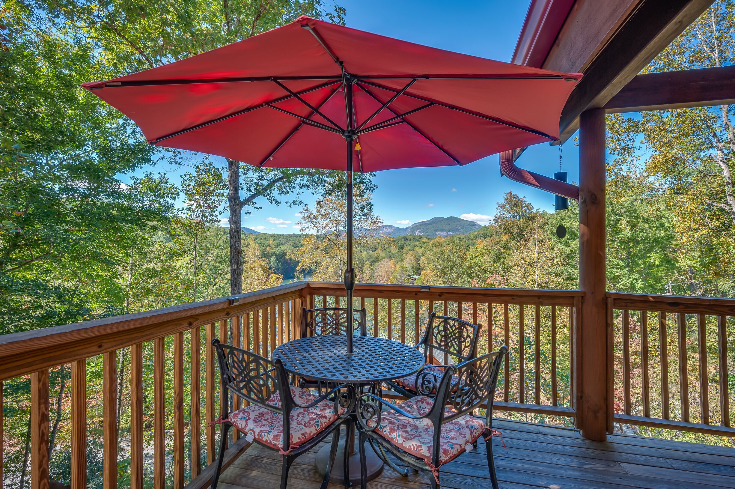 A wooden deck with a table and chairs under a red umbrella, overlooking a forested landscape.