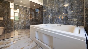 Un baño moderno con una bañera grande, paredes de mármol y una cabina de ducha de vidrio.
