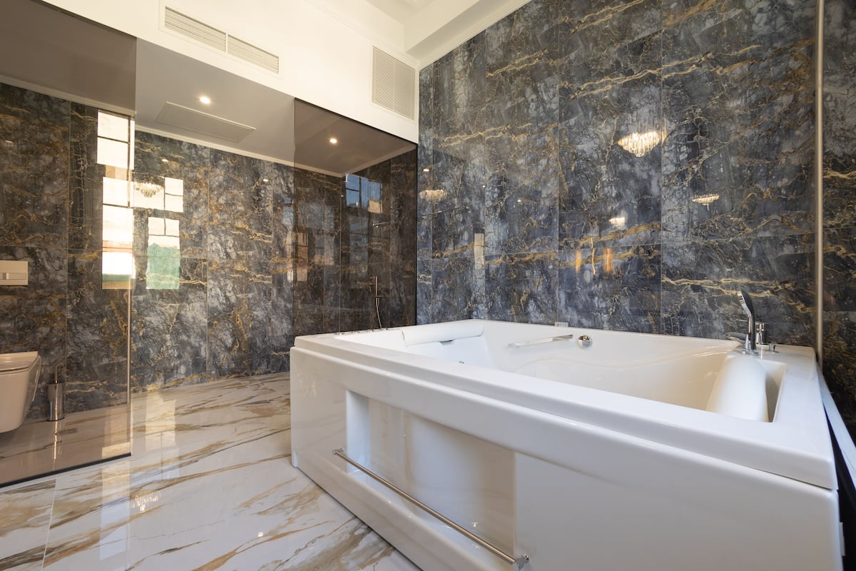 Un baño moderno con una bañera grande, paredes de mármol y una cabina de ducha de vidrio.