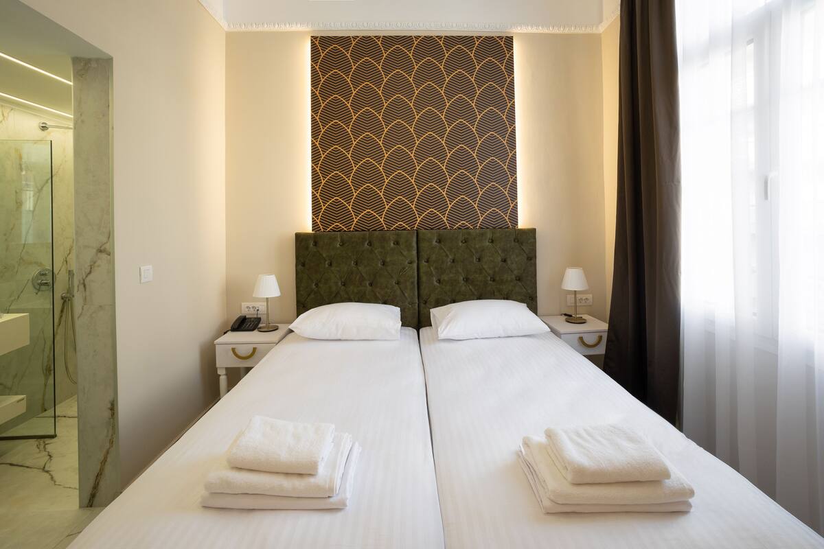Habitación de hotel con dos camas, zona de ducha de mármol y pared con diseño.