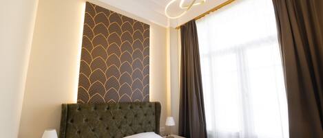 Une chambre d’hôtel avec un grand lit, une table de chevet avec une lampe, un mur orné d’un motif géométrique et une fenêtre avec des rideaux.