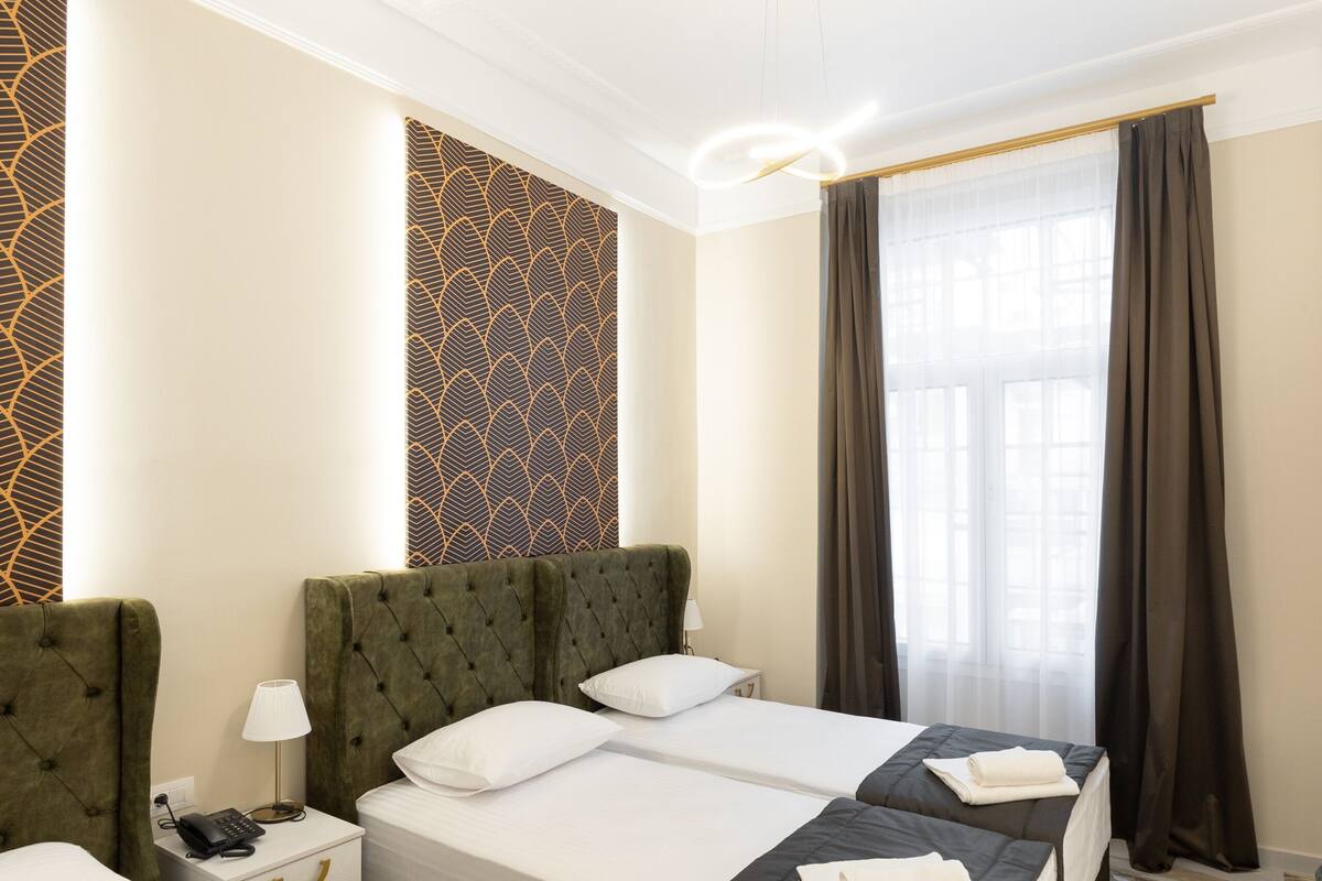 Habitación de hotel con una cama grande, una mesita de noche, una lámpara y un ventanal con cortinas.