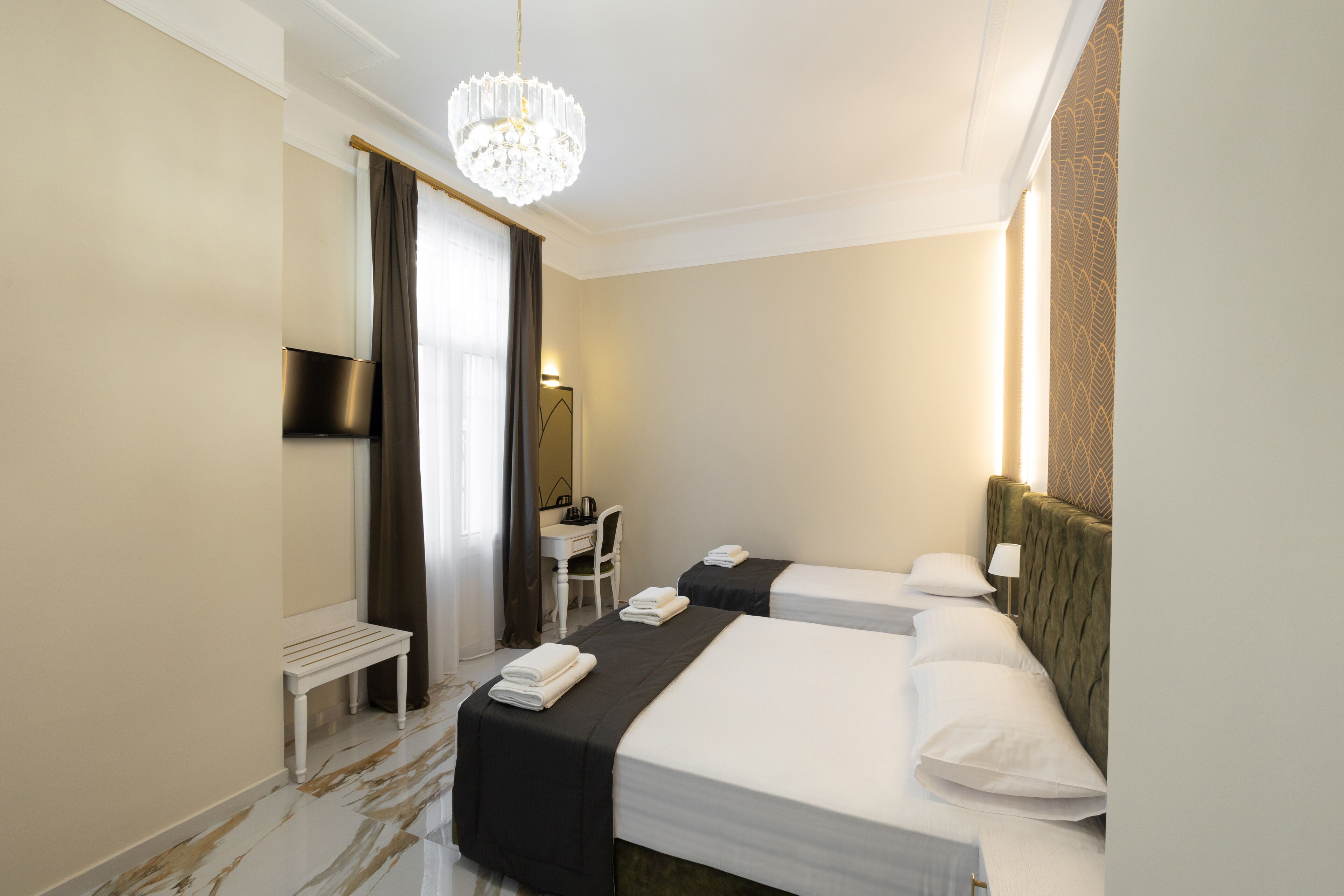 A hotel room with two beds, a desk, a chair, and a chandelier.