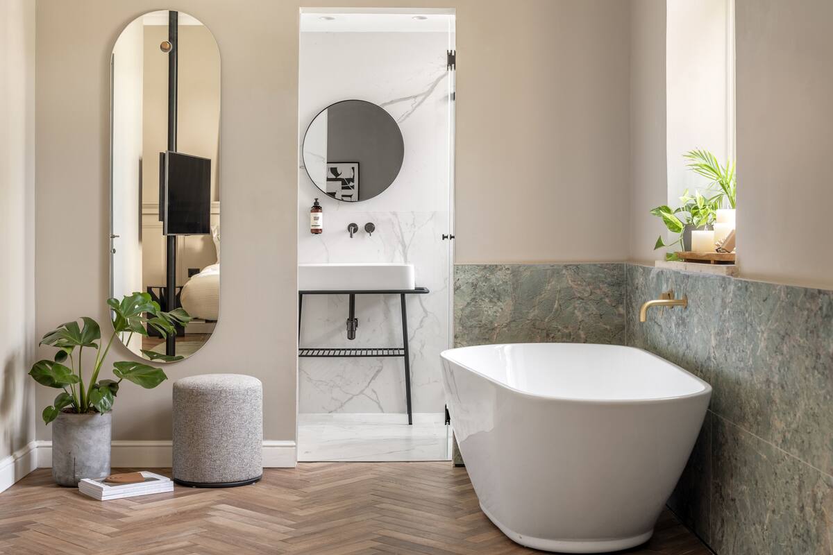 A modern bathroom with a freestanding bathtub, a round mirror, a sink with a marble countertop, and a potted plant.