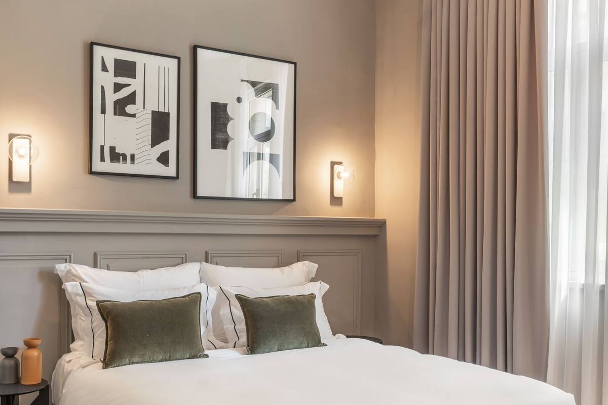 A modern bedroom with a large bed, two wall-mounted light fixtures, and a window with curtains.