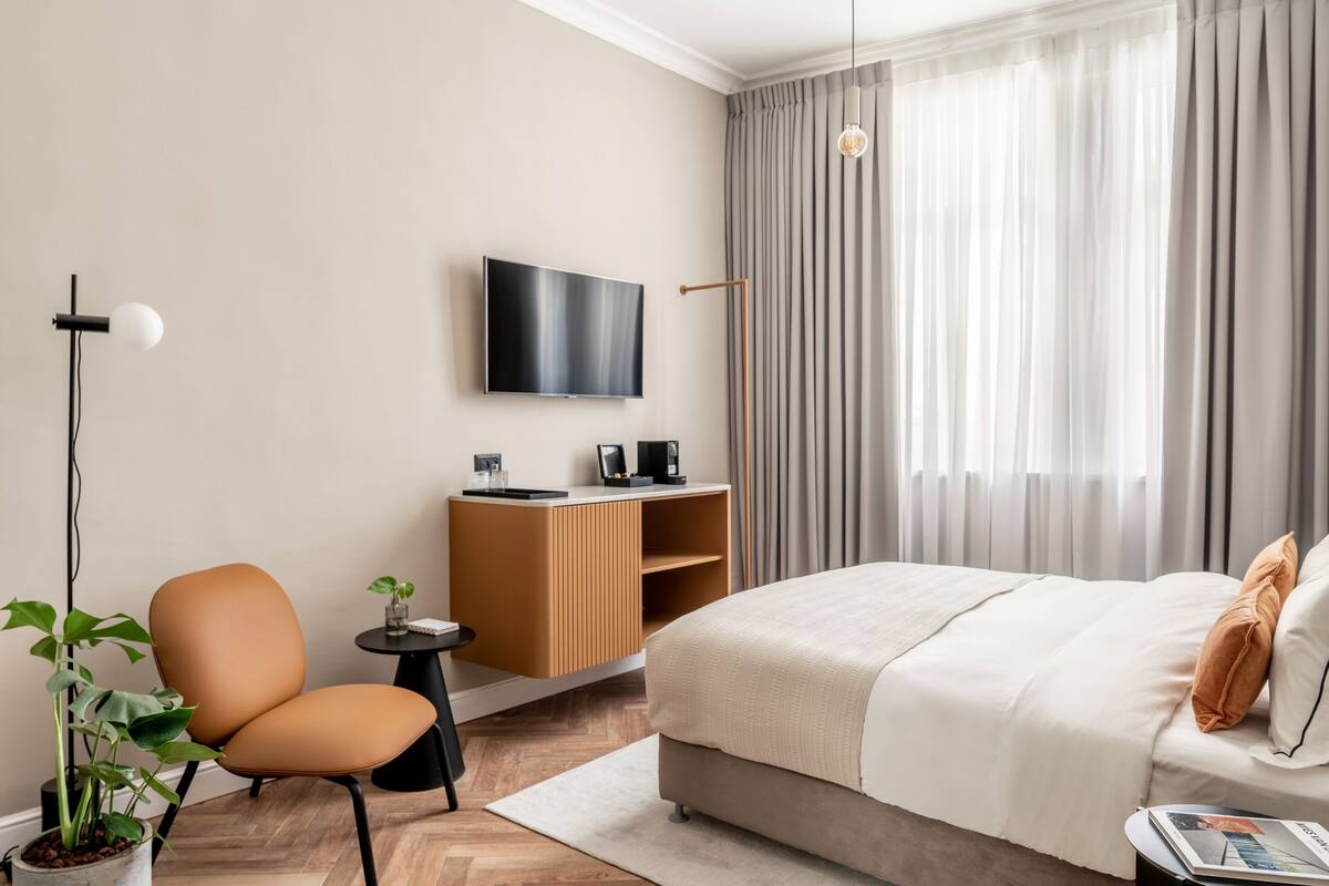 A modern hotel room with a bed, a TV, a desk, and a chair.