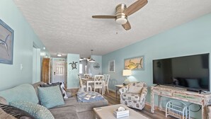 Ein Wohnzimmer mit Sofa, Sessel, Couchtisch, Fernseher und Deckenventilator.