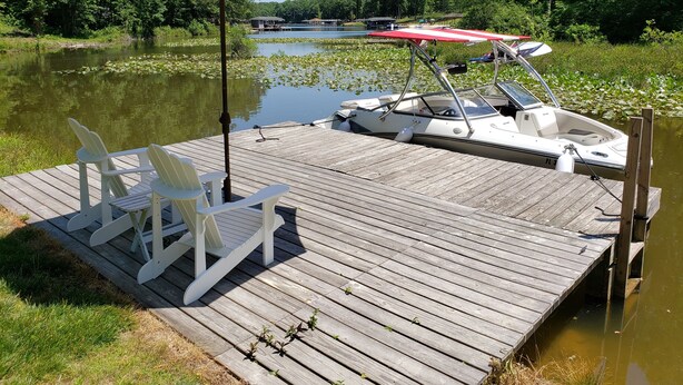 Een houten steiger met een boot, een rij witte stoelen en een grote parasol.