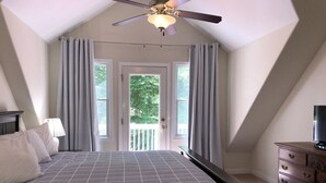Een slaapkamer met een bed, een dressoir, een plafondventilator en een deur die uitkomt op een balkon.