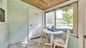 A room with a wooden ceiling, a window with a view of the outside, a door labeled "Laundry," a small round table with a pitcher, and two chairs with floral upholstery.