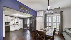A modern kitchen with white cabinets, a dining area with a wooden table and chairs, and a ceiling fan.