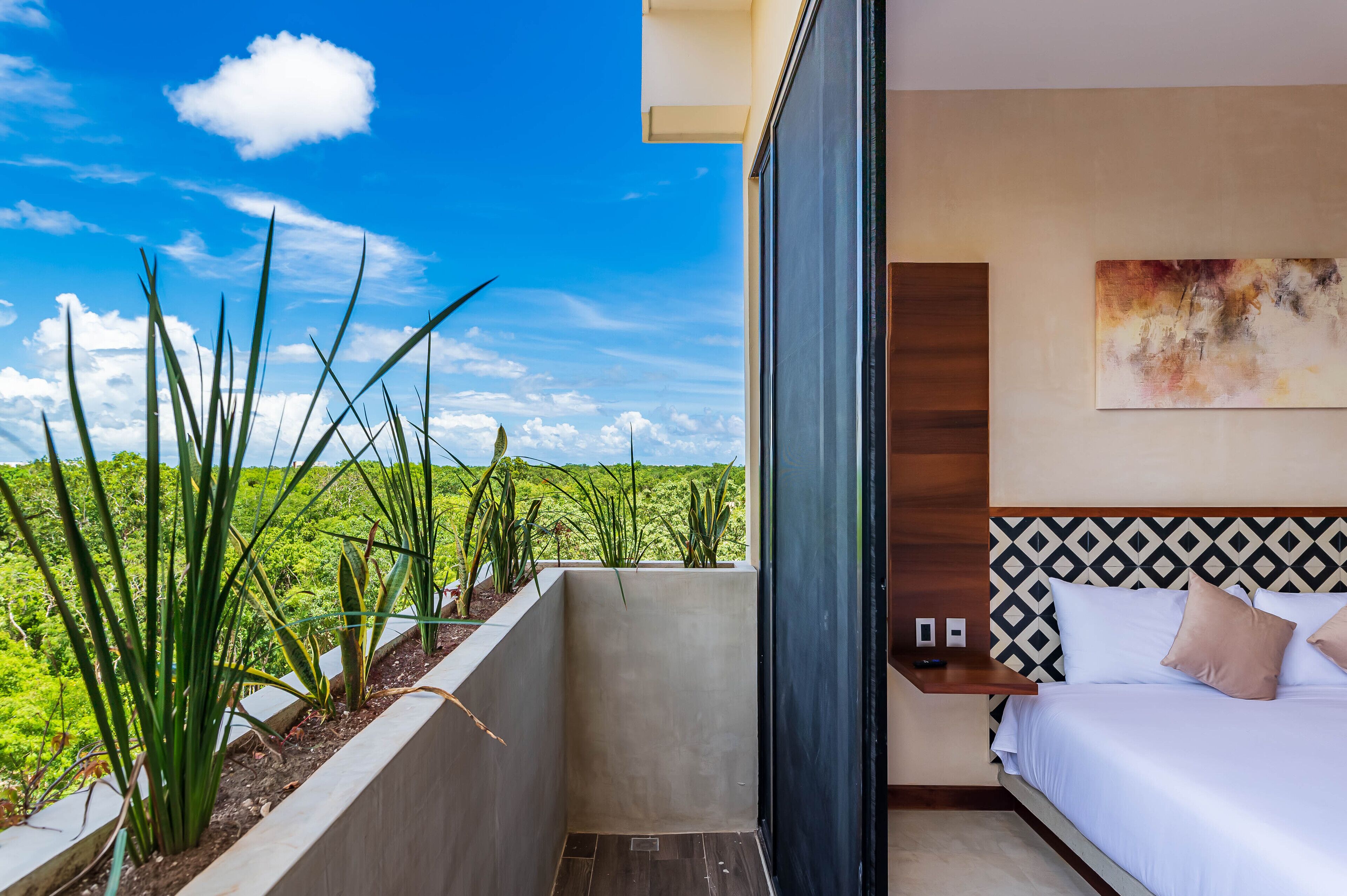 Habitación de hotel con cama, mesita de noche y vista a un paisaje verde exuberante.
