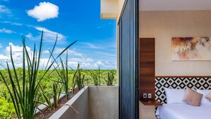 Quarto de hotel com cama, mesa de cabeceira e vista para uma paisagem verde exuberante.