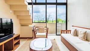 Uma sala de estar moderna com televisão, móveis de madeira, um sofá e uma grande janela com vista para o verde.