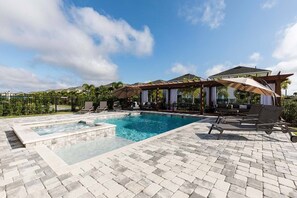 A pool area with lounge chairs and umbrellas, surrounded by a brick patio and a pergola.