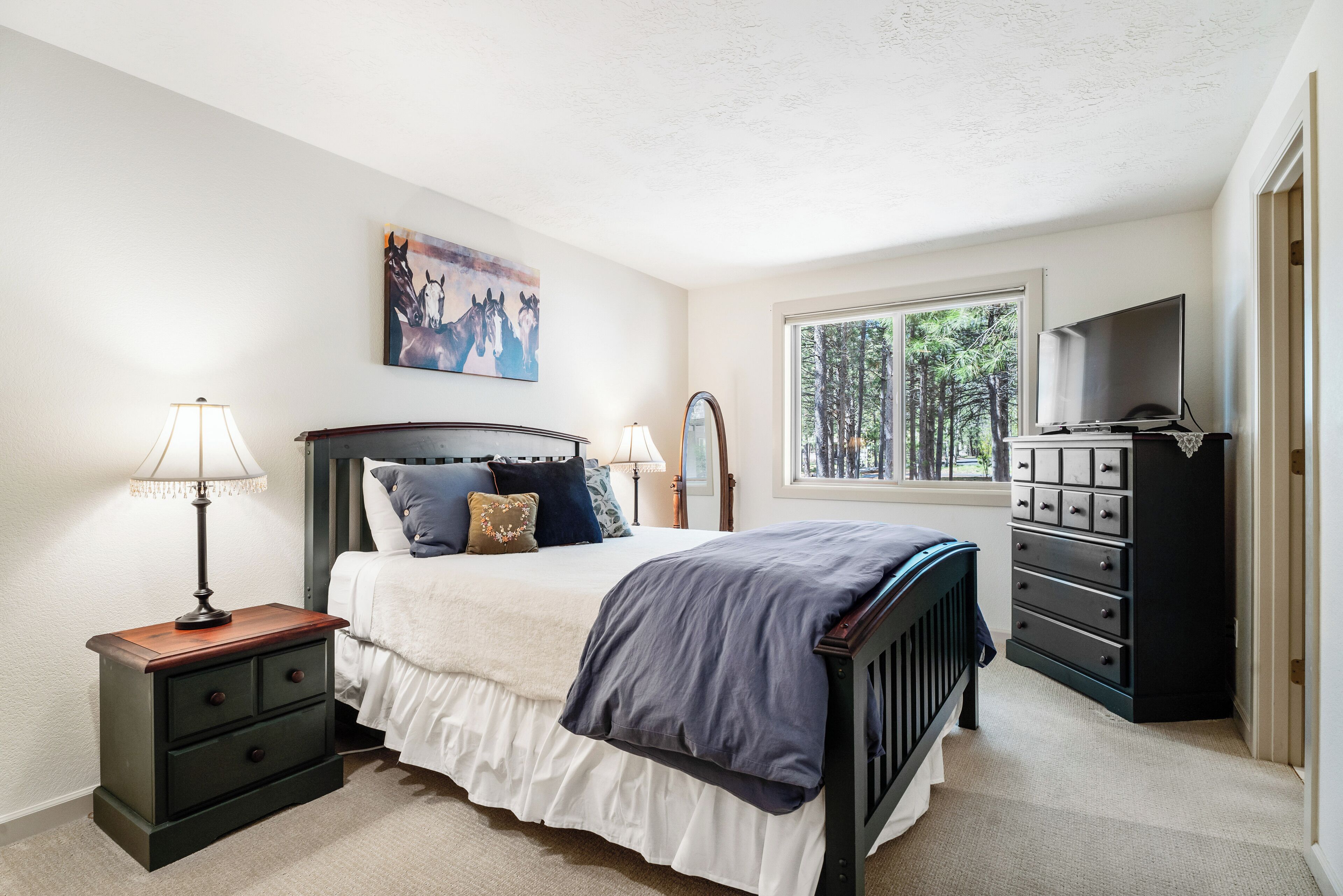 A bedroom with a bed, nightstand, dresser, and a painting on the wall.