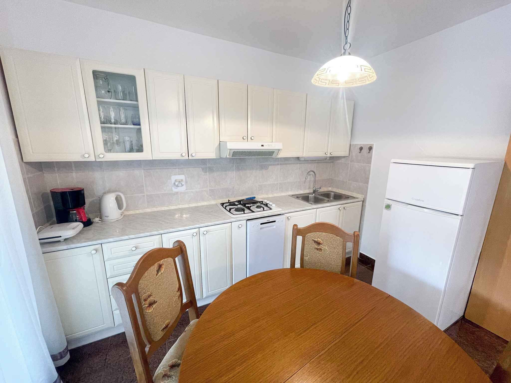 A compact kitchen with white cabinets, a gas stove, a sink, and a refrigerator.