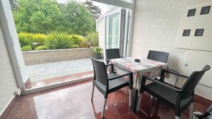 En lille patio med bord og stole, en skydedør samt udsigt til grøn vegetation.