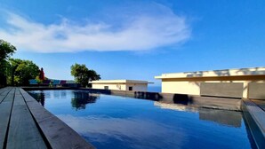 A swimming pool with a wooden deck, surrounded by buildings with a modern design. - Exceptional sea view villa with pool (Conca)