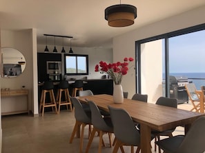 Una cuina moderna amb zona de menjador, grans finestres i vista al mar.