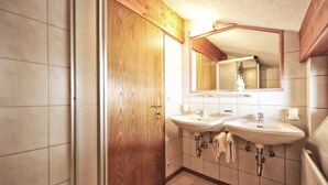 A bathroom with two sinks, wooden door, tiled walls, and a mirror above the sink. - EULE by Summit Residence (Serfaus)