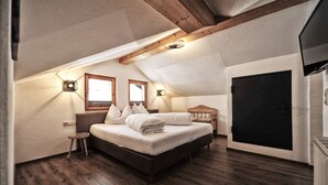 A bedroom with a wooden ceiling, a bed with pillows, a small stool, and a black door. - EULE by Summit Residence (Serfaus)