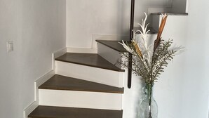 A staircase with white walls and dark wooden steps, leading to a landing with a glass vase of dried flowers.