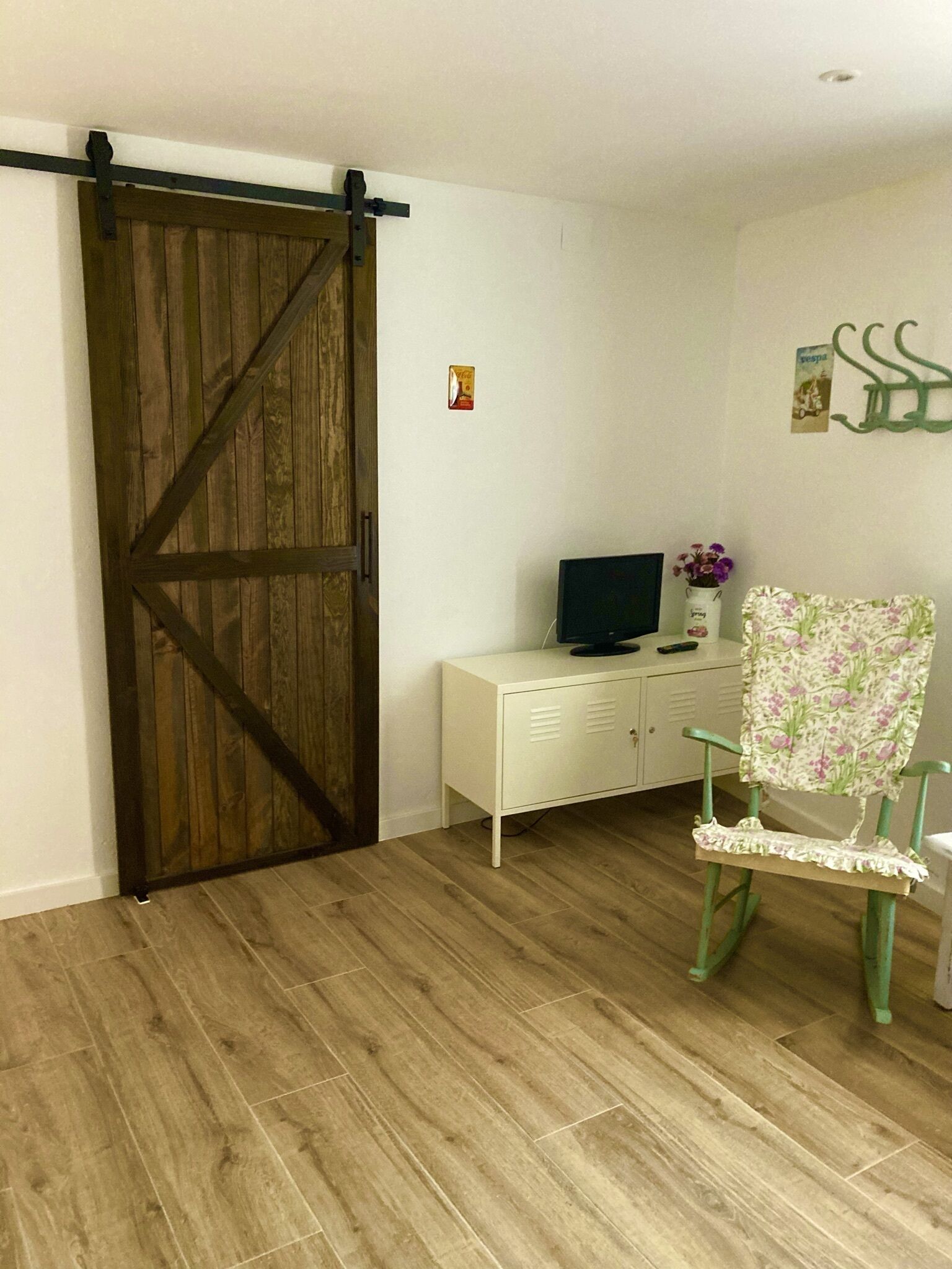 Une pièce dotée d’une porte coulissante en bois, d’un meuble blanc sur lequel se trouve un téléviseur, et d’un fauteuil à motifs floraux.