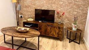 A modern living room with a stone wall, a wooden entertainment unit, a flat-screen TV, a small table with a basket, and two side tables with vases.