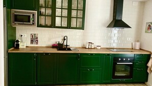 A kitchen with green cabinets, a microwave, a sink, a coffee maker, and a stove.