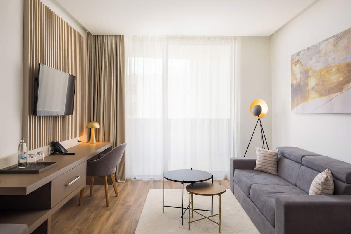 Een moderne hotelkamer met een flatscreen televisie aan de muur, een bureau met een lamp, een sofa en een klein rond tafeltje.