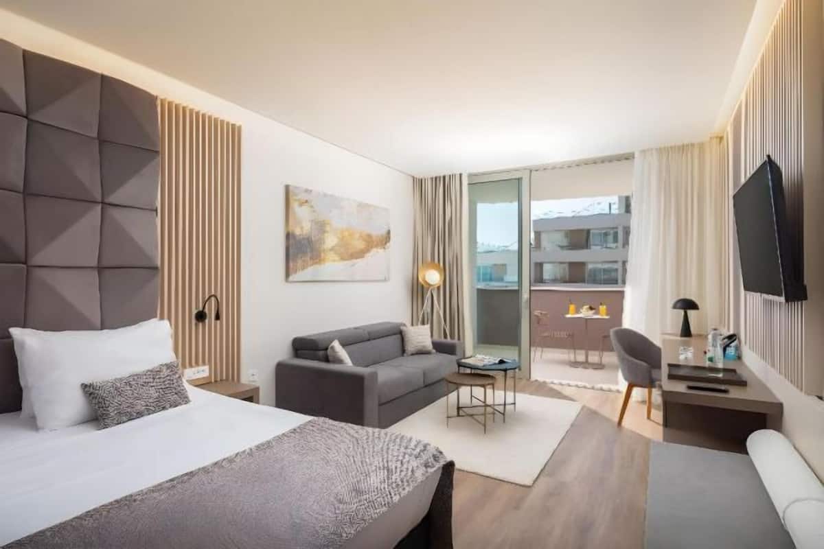 Een moderne hotelkamer met een bed, bank, televisie en balkon met uitzicht op de stad.