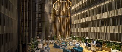 A spacious lobby with modern furniture, a high ceiling, and a large vertical wooden panel wall.