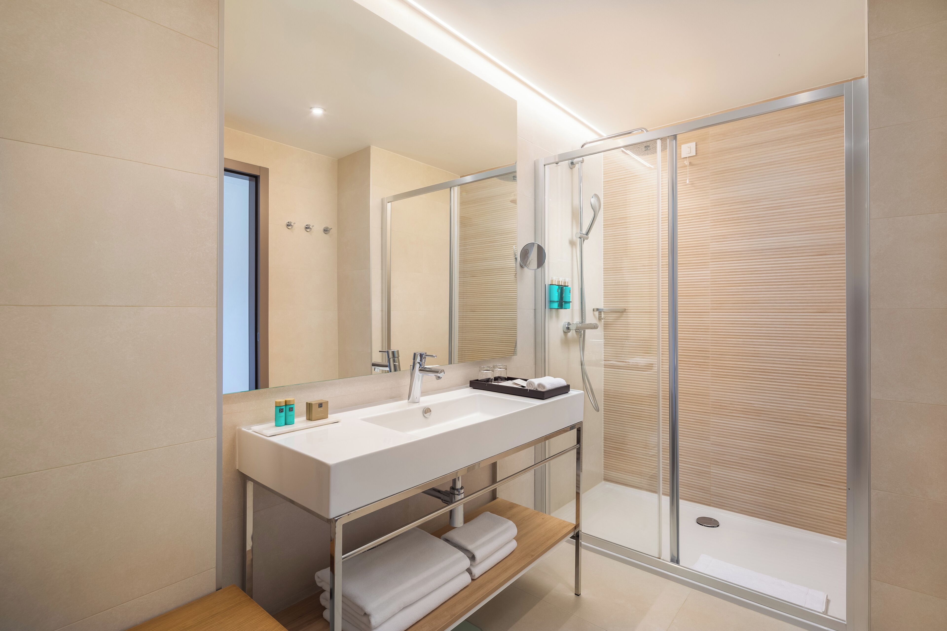 Ein modernes Badezimmer mit großem Spiegel, Waschbecken, Dusche und Handtuchhalter.