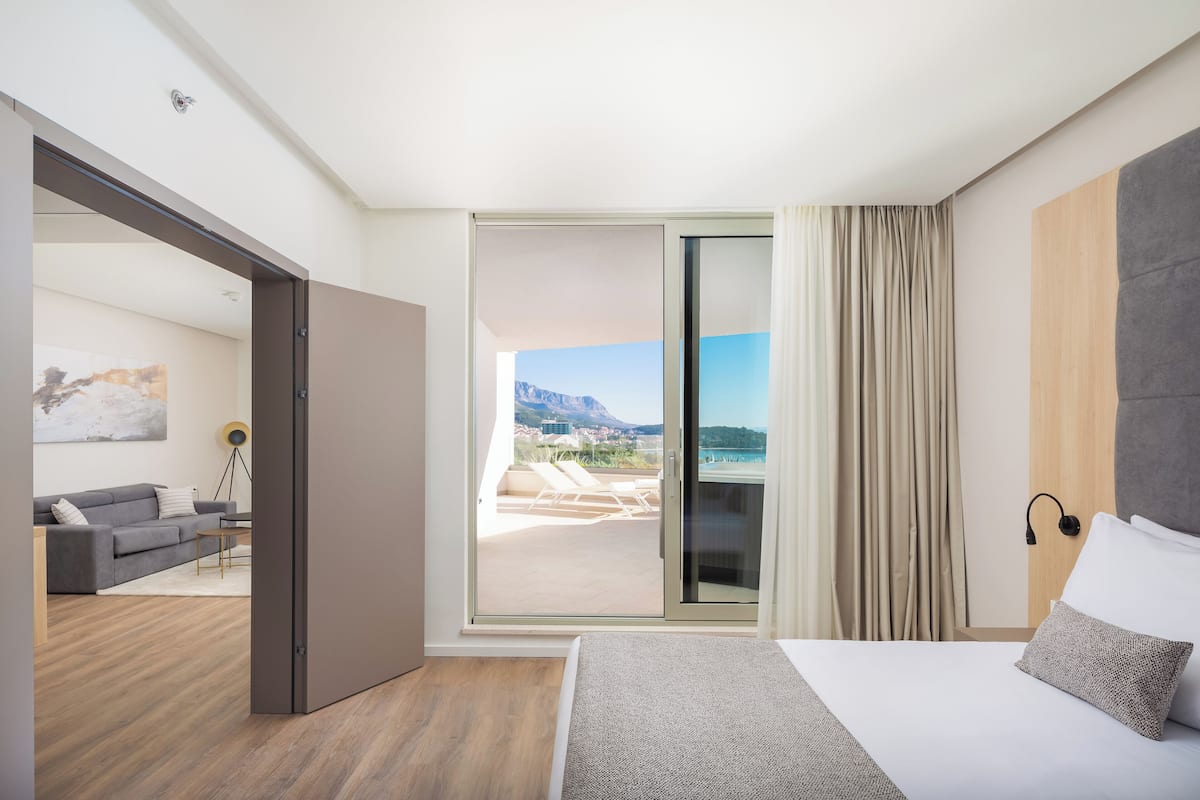 Een moderne hotelkamer met een groot bed, een balkon met uitzicht op de bergen, en een apart zithoekje met een bank en een salontafel.
