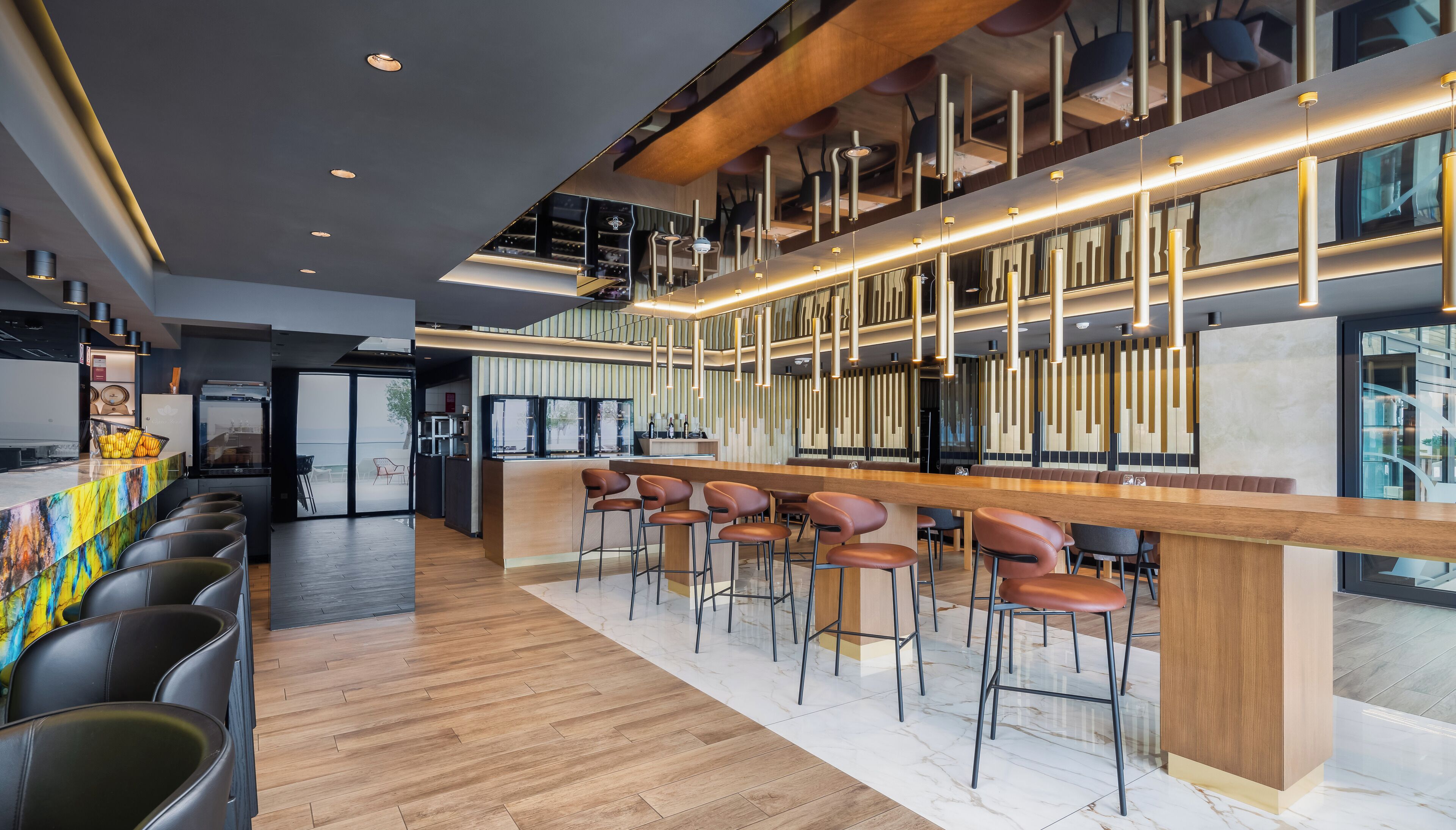 Un espace bar moderne doté d’un long comptoir, de nombreux tabourets, d’un plafond haut avec des poutres apparentes et un éclairage suspendu.
